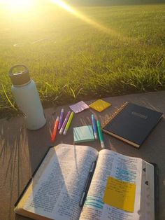 an open book sitting on top of a sidewalk next to a cup and some writing utensils