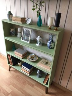 a green bookcase with books and vases on top, next to a wall