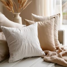 pillows and blankets on a window sill in front of a vase with dried grass