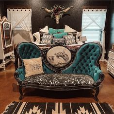 an ornate couch in the middle of a room with black walls and wooden floors, white curtains, and blue upholstered furniture