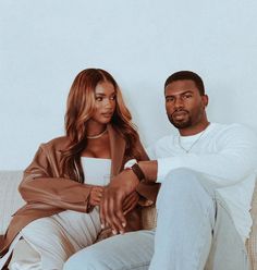 a man sitting next to a woman on top of a couch in front of a white wall