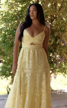 a woman wearing a yellow dress standing in front of a tree with her hands on her hips