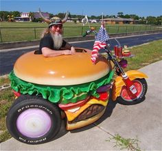 a man sitting on top of a giant hamburger shaped motorcycle with an american flag in the back