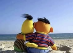 two stuffed animals sitting on top of a sandy beach