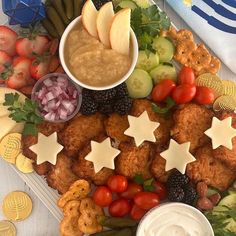 a platter filled with crackers, fruit and vegetables next to some dips