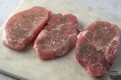 three raw pork chops on a cutting board with seasoning sprinkles