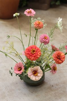 an arrangement of flowers in a green vase on the ground next to potted plants