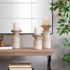 three candles are sitting on a table with books and a mirror in the back ground