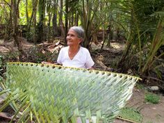 an older woman standing in the woods holding a large piece of green grass that has been woven into it