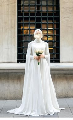 a woman in a white gown and veil holding a bouquet with flowers on the street