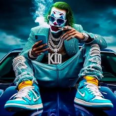 a man with green hair and clown makeup sitting on top of a blue car holding a cell phone