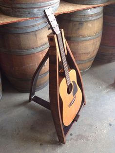 an acoustic guitar is sitting on a stand in front of some wine casks and barrels