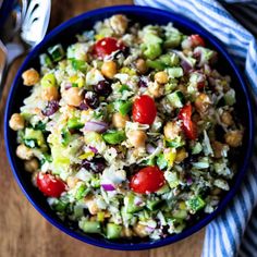 a blue bowl filled with salad on top of a wooden table next to a fork