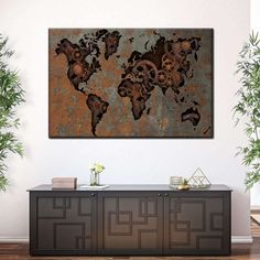 a metal world map hanging on a wall in a room with plants and potted plants