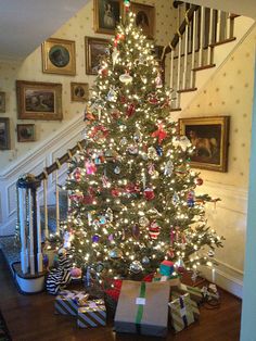 a christmas tree with presents under it in front of stairs and pictures on the wall