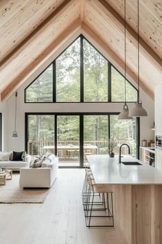 an open living room and dining area in a house with wooden ceilings, white furniture and large windows