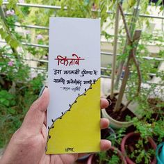 a person holding up a piece of paper with writing on it in front of some plants