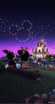 mickey and minnie mouse sitting in front of a castle at night with the lights on