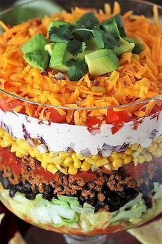 layered mexican salad in a glass dish with tortilla chips and avocado