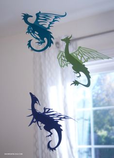 three paper cut dragon mobiles hanging from the ceiling in front of a white curtain