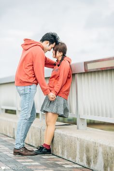 a man and woman standing next to each other on a cement wall near a bridge