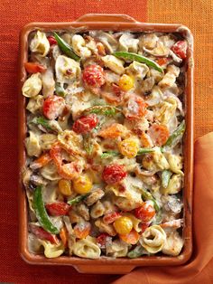 a casserole dish filled with pasta, tomatoes and green beans on a red cloth