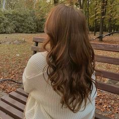 a woman sitting on top of a wooden bench in front of a park filled with trees