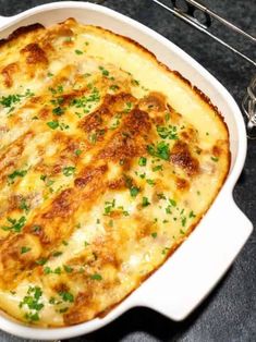 a casserole dish with cheese and parsley in it on a black table