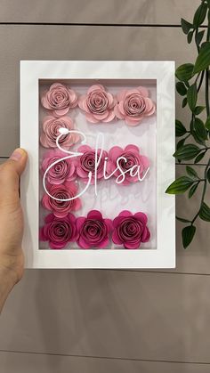 a person holding up a framed photo with pink roses in the frame and personalized name on it