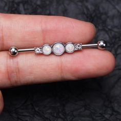 a person is holding an opal barbell ring with three balls on the end