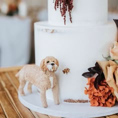 a dog figurine sitting on top of a white tiered cake with flowers