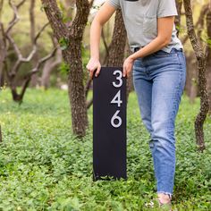 a woman standing next to a black sign in the grass with numbers printed on it