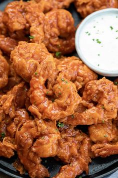 a black plate topped with fried chicken next to a small bowl of ranch dressing on the side