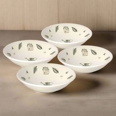 three white bowls with green designs on them sitting on a brown tableclothed surface