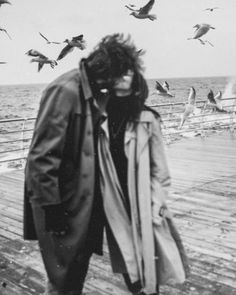 a man standing on a pier with birds flying over him and the ocean in the background