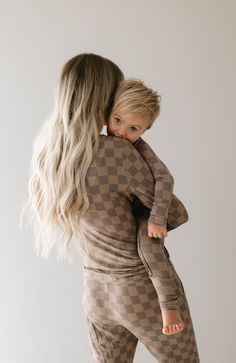 a woman holding a child in her arms while she is wearing brown checkered pajamas