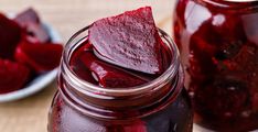 a jar filled with beets sitting on top of a wooden table next to another jar