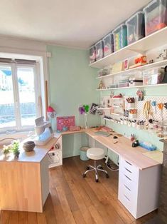 a room with a desk and shelves filled with crafting supplies on the wall next to a window