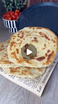 three flatbreads stacked on top of each other in front of a bowl of tomatoes