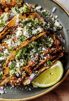 some tacos are sitting on a plate with lime wedges and cilantro