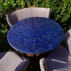 a blue table and chairs sitting in the grass near some bushes with green plants behind it