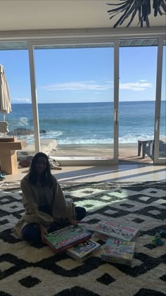 a woman sitting on the floor reading a book in front of an open window overlooking the ocean