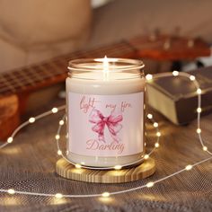 a lit candle with a pink bow on it sitting next to a string of lights