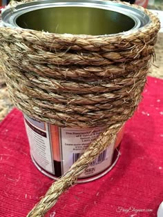 a tin can with some straw wrapped around it on a red table cloth next to other items