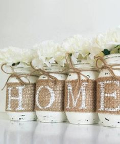 four mason jars with the word home painted on them are lined up in front of white flowers