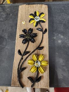 two yellow and black flowers are sitting on a piece of wood with beads in the middle