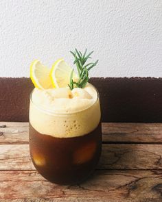 a drink with lemon and rosemary garnish in a glass on a wooden table