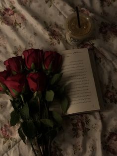 a bouquet of red roses sitting on top of a bed next to an open book