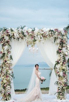 a woman in a wedding dress standing under an arch with flowers and greenery on it