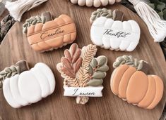 decorated cookies sitting on top of a wooden table next to white pumpkins and leaves